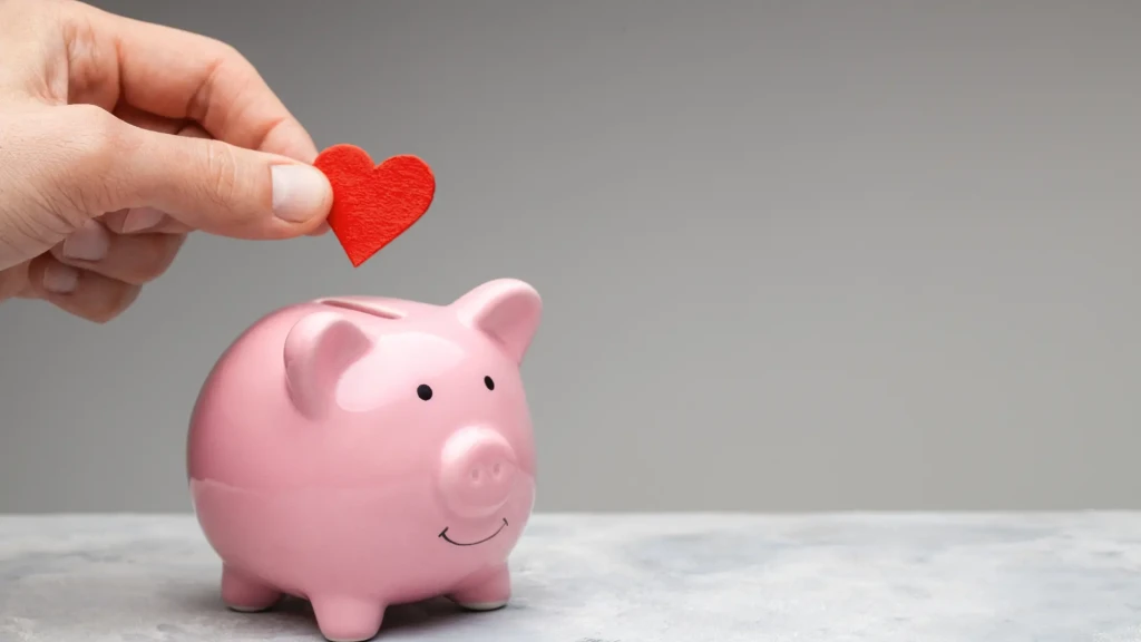 Main insérant cœur dans tirelire, budget micro-crèche 2025, coûts d'ouverture et investissement - Blog expert micro-crèche La Girafe Verte